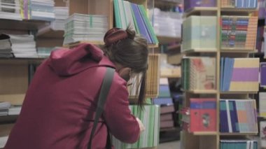 Virüse karşı gözlük ve maske takan kadın kırtasiye dükkanından defter satın alıyor.