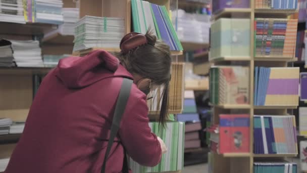 Mujer con gafas y máscara contra el virus compra cuadernos en la tienda de papelería — Vídeos de Stock