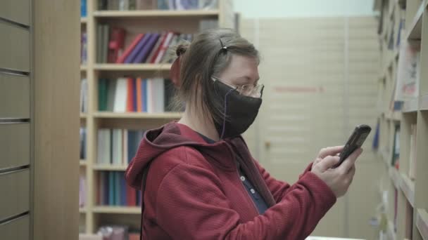 Woman in glasses and mask against virus takes photos of bookshelves in bookstore — Stock Video