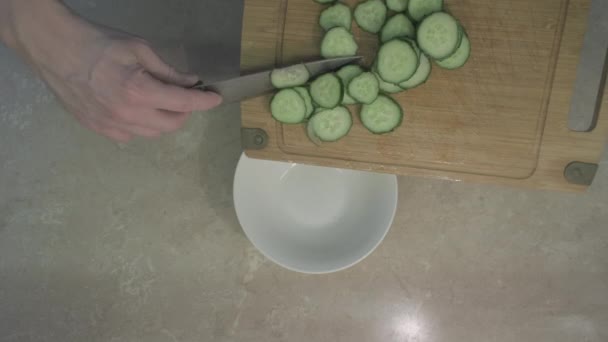 El hombre pone los pepinos cortados en círculos para la ensalada en un plato. De cerca. — Vídeos de Stock