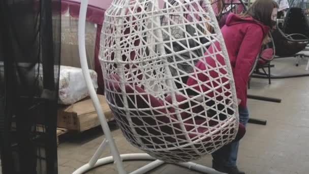 Женщина в маске против вируса выбирает гамак в виде гнезда в магазине — стоковое видео