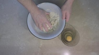 Erkek eli hamuru yoğurur, sonra yumurtaya ekler ve yoğurmaya devam eder.