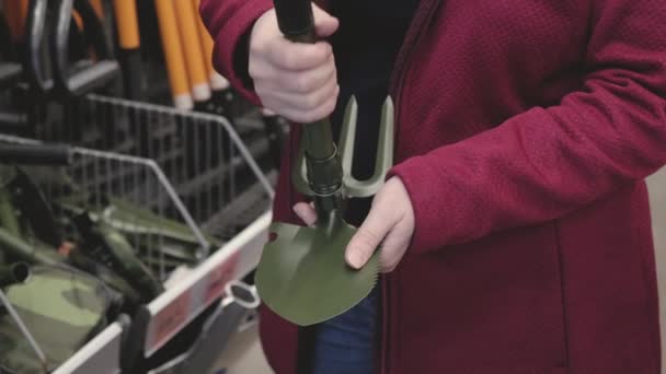 Mujer en la tienda elige un plegable, pala turística con un rastrillo — Vídeos de Stock