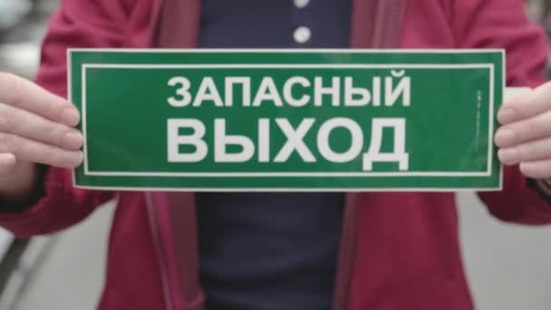 女性はロシアのキリル文字の碑文の緊急出口を持つ記号を保持します。閉じろ! — ストック動画