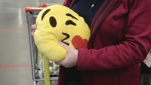 Jente i butikken kjøper en rar pute i form av gult smilefjes for bilsetet – stockvideo