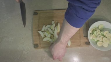 Adam armudu dilimliyor ve elma ve muzla birlikte koyuyor. Tatlı, meyve salatası yapmak için.