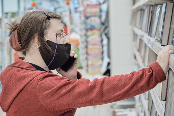 Virüse karşı maskeli kadın telefonda konuşuyor ve kitapçıdan bir kitap seçiyor.