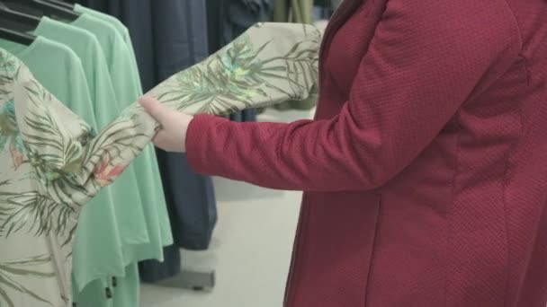 Mujer con sobrepeso elige camisa con patrón de palmera tropical en la tienda de ropa — Vídeos de Stock