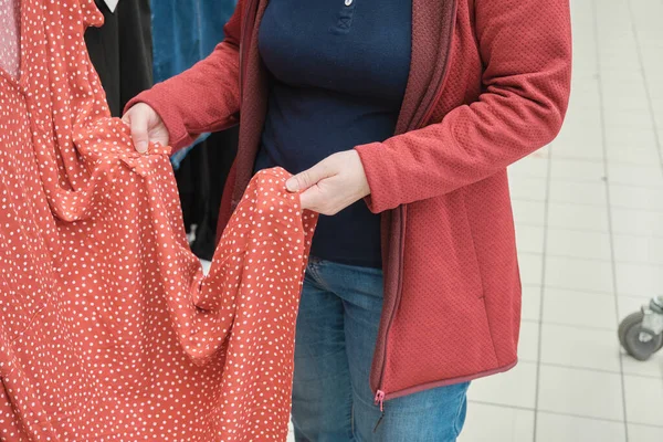 Ciężarna kobieta w sklepie decyduje się kupić przestronną czerwoną sukienkę z białymi kropkami polki — Zdjęcie stockowe