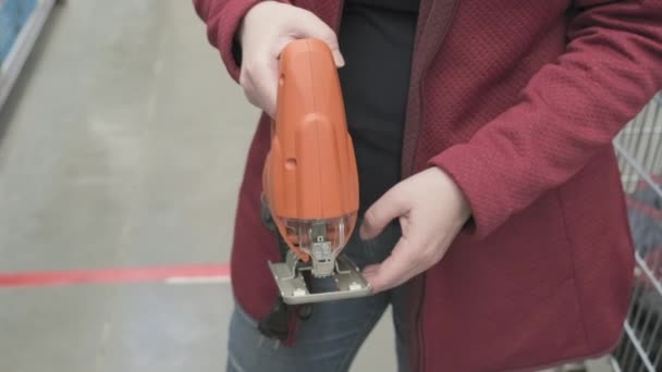 Mulher em uma loja de materiais de construção escolhe comprar um quebra-cabeça elétrico. Fechar — Vídeo de Stock