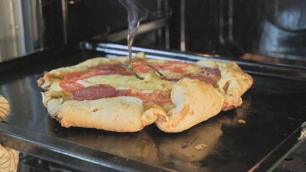 Ręka Mans wyciąga z piekarnika brzydką, krzywą pizzę w stylu country — Zdjęcie stockowe