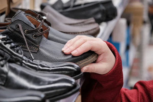 Mulher em uma loja de roupas escolhe sapatos de couro patente sob um terno de negócios — Fotografia de Stock