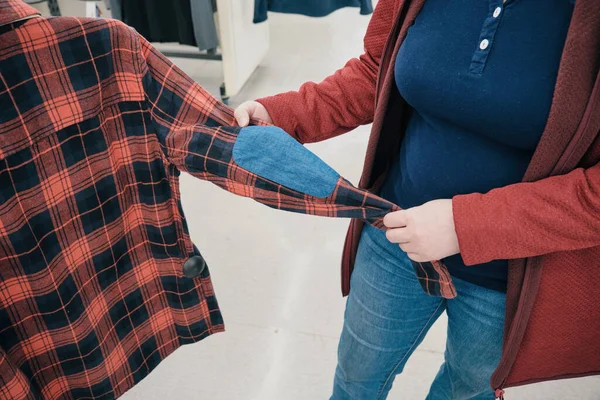 Mulher grávida escolhe camisa xadrez flannelette na loja para comprar. Mãos ao alto — Fotografia de Stock