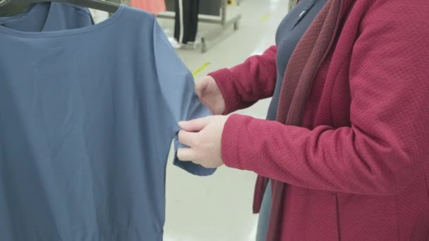 Кавказька вагітна жінка вибирає блакитну блузку в магазині. Руки закриваються. — стокове відео