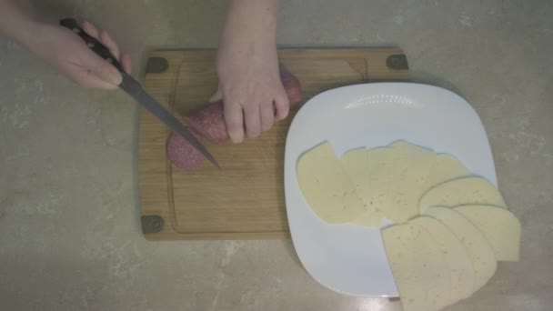 Mulher fatia salsicha defumada com faca e coloca-o no prato ao lado de queijo — Vídeo de Stock