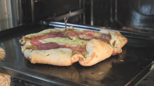 Mans handschoen hand trekt een lelijke, scheef land stijl pizza uit de oven — Stockvideo