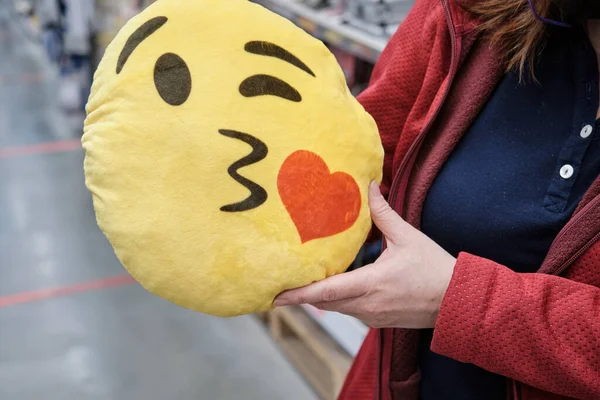 Chica en la tienda compra almohada divertida en forma de cara sonriente amarilla para asiento de coche —  Fotos de Stock