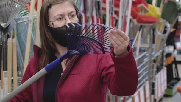 Kobieta w sklepie kupuje miotłę do zbierania opadłych liści. Nosi maskę. — Wideo stockowe