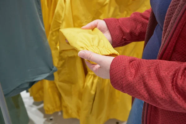 Mulher grávida caucasiana escolhe blusão amarelo da chuva na loja para comprar — Fotografia de Stock