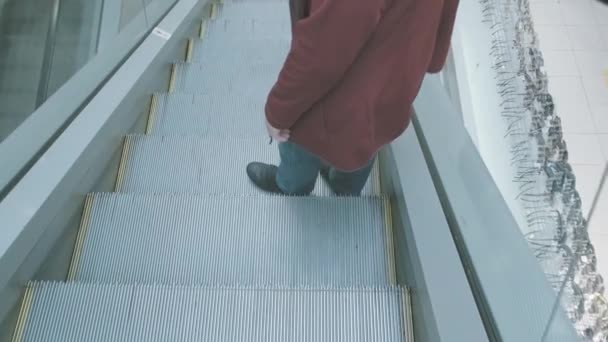 Běloška v červené bundě jde dolů po železném eskalátoru v obchoďáku — Stock video