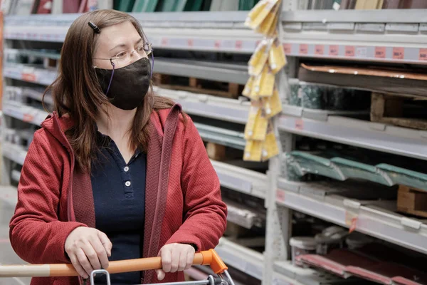 Woman with glasses rides through building materials store with grocery cart