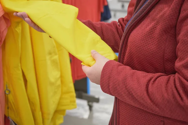 Mulher caucasiana escolhe blusão amarelo da chuva na loja para comprar — Fotografia de Stock