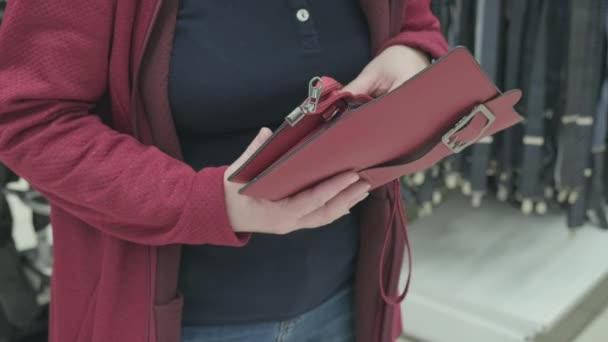 Eine Frau in einem Geschäft sucht sich eine rote Clutch zum Kauf aus. Nahaufnahme mit den Händen — Stockvideo