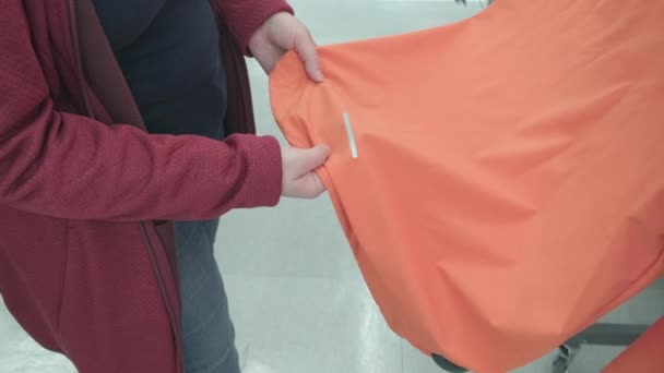 Mujer embarazada elige chaqueta naranja con franja reflectante en la tienda para comprar — Vídeo de stock