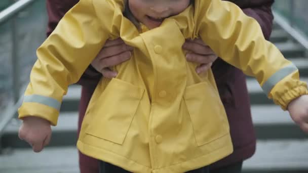 Mère prend un enfant dans une veste jaune avec une capuche dans les bras — Video