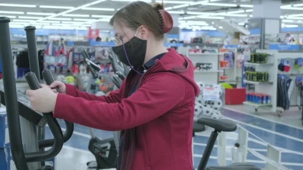 Γυναίκα σε ένα κατάστημα αθλητικών επιλέγει ένα μεγάλο προσομοιωτή σπορ - διάδρομο για να αγοράσει — Αρχείο Βίντεο