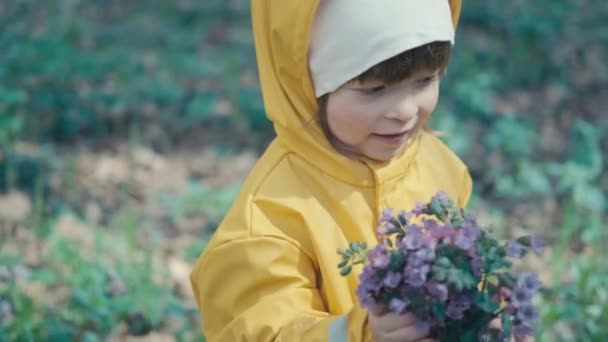 Klein meisje in gele regenjas met kap geeft haar moeder boeket bloemen — Stockvideo