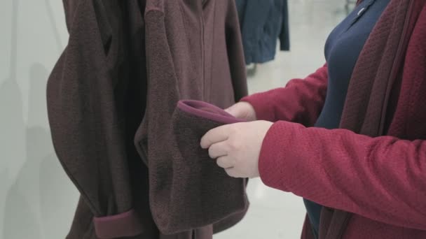 Zwangere vrouw kiest fleece bordeaux jas met capuchon jas in de winkel te kopen — Stockvideo