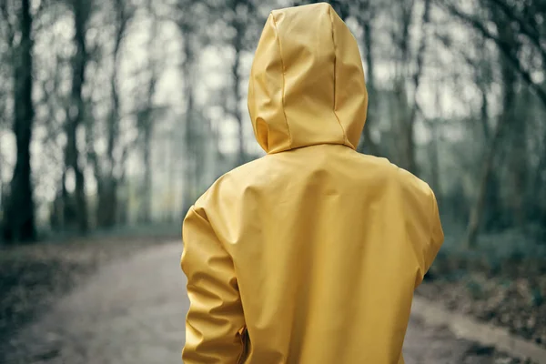 Man in a yellow raincoat with a hood stands on the road in a dark scary forest