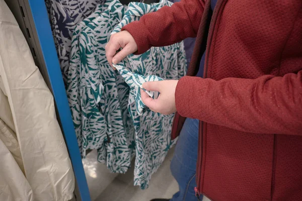 Kobieta wybiera zieloną koszulę z tropikalnym wzorem drzewa w sklepie odzieżowym kupić — Zdjęcie stockowe