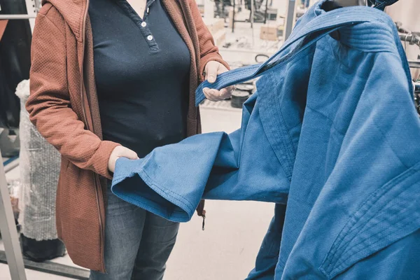 Mulher na loja escolhe comprar kimono azul para o wrestling. Mãos de perto tiro — Fotografia de Stock