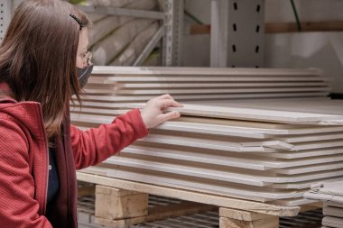 Virüse karşı maskeli bir kadın inşaat malzemeleri mağazasından fiberboard alıyor.