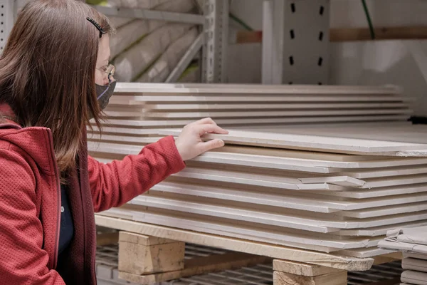 Virüse karşı maskeli bir kadın inşaat malzemeleri mağazasından fiberboard alıyor.
