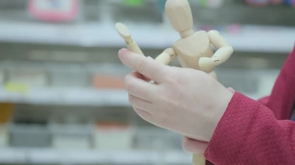 Vrouw in een winkel kiest ervoor om een beeldje van een houten man te kopen. Handen van dichtbij. — Stockvideo