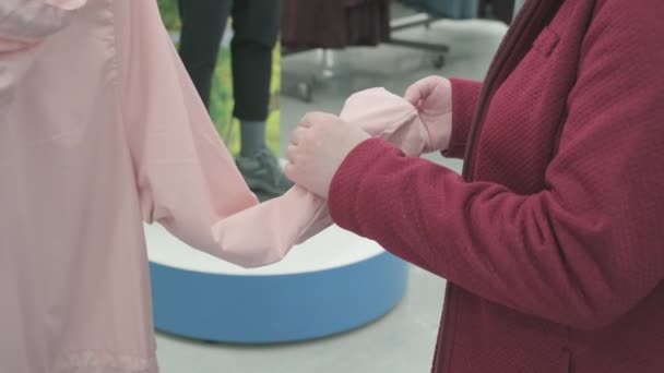 Λευκή γυναίκα επιλέγει ροζ μπουφάν αντιανεμικό από τη βροχή στο κατάστημα για να αγοράσει — Αρχείο Βίντεο