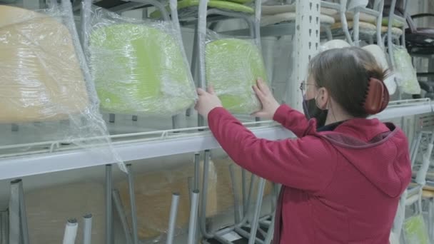 Женщина в маске против вируса выбирает новое светло-зеленое кресло для покупки — стоковое видео