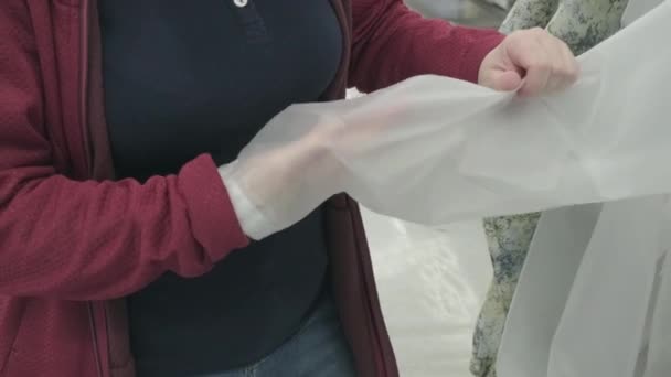 Caucasian woman chooses transparent windbreaker jacket from rain in store to buy — Stock Video
