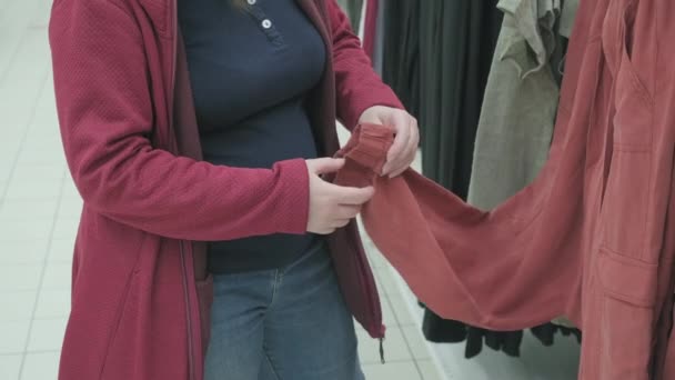 Schwangere entscheidet sich im Laden für lockere rote Hosen. Nahaufnahme mit den Händen — Stockvideo