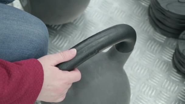 Een vrouw in een winkel kiest voor een gewichtheffen kettlebell. Handen van dichtbij. — Stockvideo