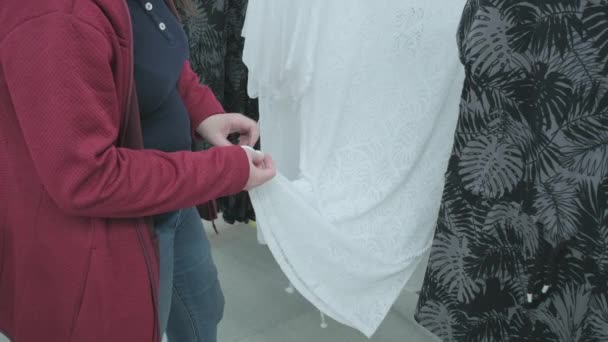 가게에 있는 임신 한 여자가 헐렁 한 흰색 레이스와 투명 한 드레스를 선택 한다 — 비디오