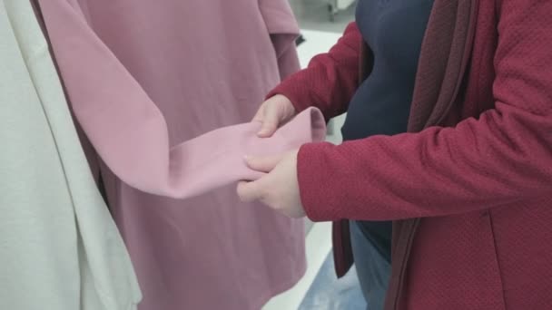 Caucasian pregnant woman chooses a spacious, pink fleece jacket in store to buy — Stockvideo