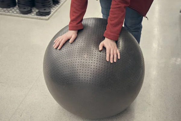 Woman in store buys fitball. She touches it with her hands testing its strength