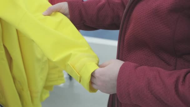 Mujer caucásica elige cortavientos amarillo de la lluvia en la tienda para comprar — Vídeos de Stock