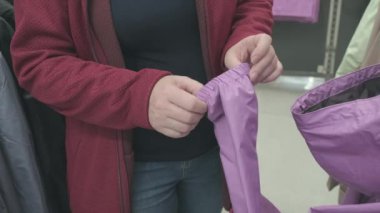 Hamile kadın mor rüzgarlık ceketi seçiyor ve dükkanda yağmurluk var.