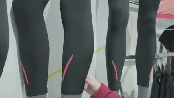 Mulher em uma loja de esportes escolhe leggings apertados e sintéticos para correr para comprar — Vídeo de Stock