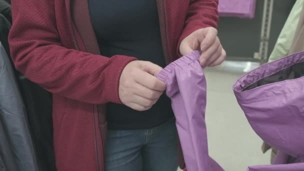 Беременная женщина выбирает фиолетовую ветровку с капюшоном дождя в магазине, чтобы купить — стоковое видео